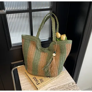 Detail of green and beige woven tote bag with fringe tassel on a stone surface