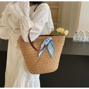 Detail of hand-woven straw bucket bag with blue-white striped ribbon and leather handle
