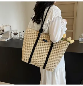 Détail d'un sac cabas tissé main en paille beige avec anses noires et logo carré chic