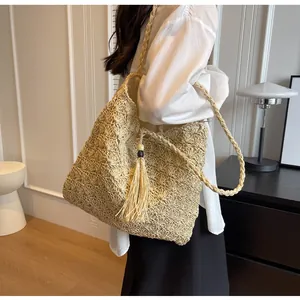 Detail of a beige woven straw tote bag featuring decorative long tassels and wood beads