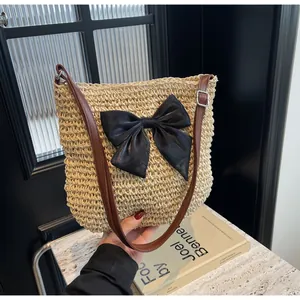 Detail der handgewebten Strohtasche mit großer schwarzer Schleife und braunem Schultergurt