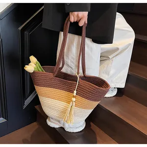 Sac de plage tressé tricolore avec pompon et sangle marron sur un escalier en bois