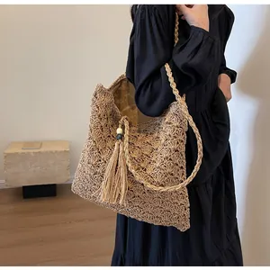 Detail of woven hollow straw tote bag featuring decorative long tassels and wooden beads