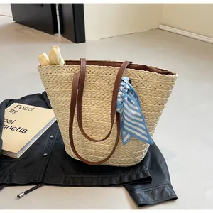 Close-up of woven straw tote bag with brown leather straps and striped silk scarf