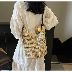 Detailweergave van een beige geweven stro-schoudertas met bruine lederen riem