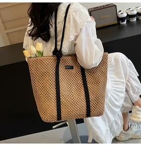 Détail d'un sac cabas en paille tissée ajourée avec anses en corde noire et patch cuir