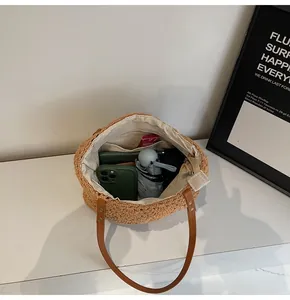 Spacious interior of woven straw tote bag with leather straps holding a phone and umbrella