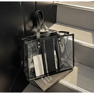 Detail of transparent PVC tote bag with black leather handles and silver rivet reinforcement