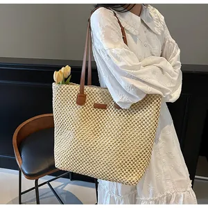 Grand sac cabas en paille tressée avec anses en cuir marron porté sur une robe blanche