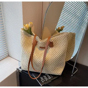 Détail du sac cabas en paille tressée beige avec anses en cuir marron sous lumière naturelle