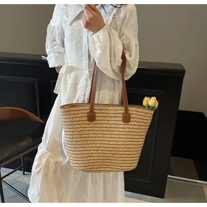 Detail of a woven straw tote bag with brown leather handles and spacious interior