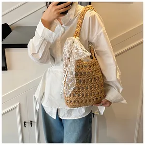 Detail der Häkel-Stricktasche mit großer weißer Spitzen-Schleife auf natürlichem Stroh
