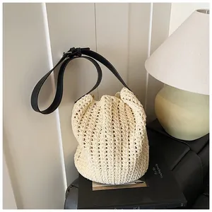 Gros plan d'un sac seau tressé beige avec bandoulière en cuir noir et boucle en métal