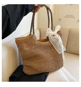 Detail of a brown woven straw tote bag featuring a white lace bow and striped handles