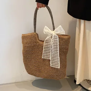 Detail of hand-woven straw tote bag with black-white striped handles and large white lace bow