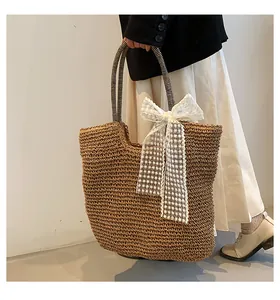 Detail of woven straw tote bag featuring a lace bow and black striped handles