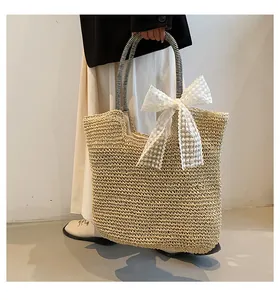 Detail of straw beach bag featuring a large white lace bow and striped handle