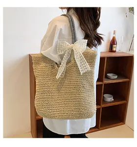 Straw tote bag detail with large white lace bow and striped strap on model side view