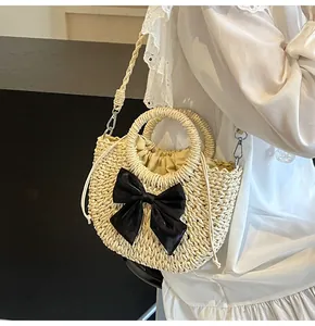 Detalle de bolso bandolera de paja tejida crema con lazo negro sobre una modelo real