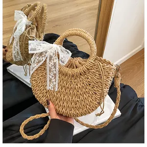 Dettaglio borsa in paglia a mezzaluna con fiocco in pizzo bianco e doppia tracolla