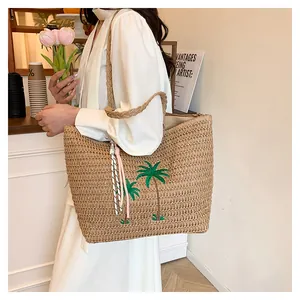 Detail of a woven straw tote bag featuring palm tree embroidery and pink tassel accents