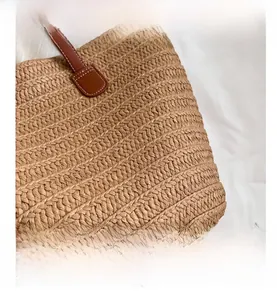 Detail of straw woven tote showing brown leather handles and premium white stitching