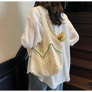 Detail of hand-knitted beige tote bag with green wave pattern carried by a model