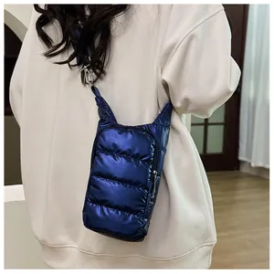 Close-up of a blue quilted puffer crossbody phone bag on model showing adjustable strap