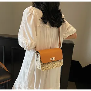 Detail of handwoven straw crossbody bag with tan leather flap and gold twist lock