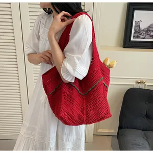 Detail of red crochet knit tote bag with green wavy edge shown on shoulder in interior