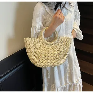 Sac de plage en paille en forme de demi-lune avec anses rondes dans un cadre de vacances