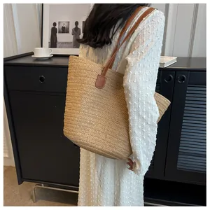 Detail showing woven straw texture and premium brown leather shoulder strap on tote bag