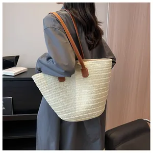 Détail d'un sac cabas en paille tissée avec bandoulières en cuir marron et texture épurée