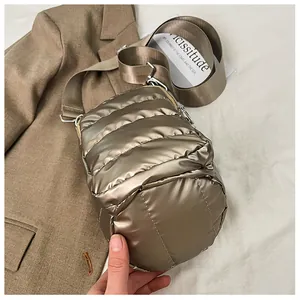 Detailed view of bronze metallic quilted crossbody bag with wide nylon strap on white fabric