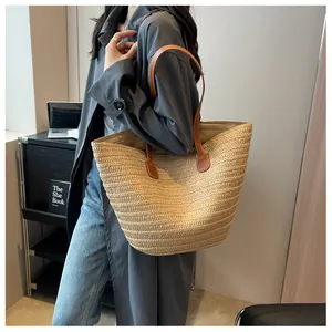 Vue détaillée du grand sac cabas en paille tressée avec anses en cuir marron porté par un mannequin