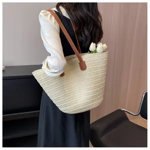 Détail du sac fourre-tout tissé crème avec anses en cuir marron sur l'épaule du mannequin