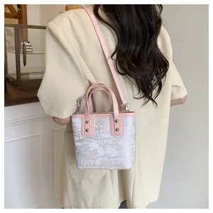 Detail of Chinese style embroidery on white bucket bag with pink leather strap handles