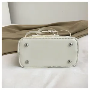 Detailed bottom view of beige embroidered bucket bag with silver protective metal feet