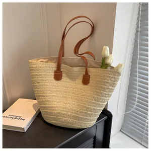 Close-up of woven straw tote bag with brown leather handles and white contrast stitching