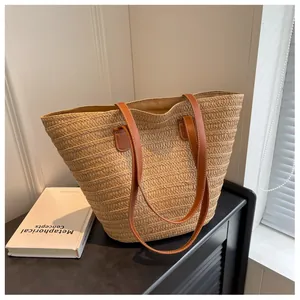 Detail of natural straw texture and brown faux leather shoulder strap on a woven tote bag