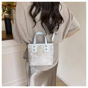 Detail of elegant beige bucket bag with gold Toile de Jouy embroidery and silver rivets