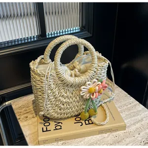 Detail of woven straw handbag featuring floral charms and drawstring closure for summer