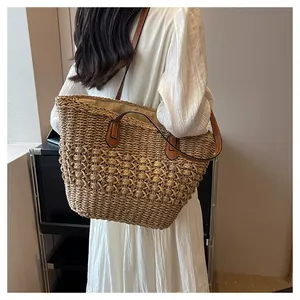 Close-up detail of the woven texture and brown leather handles on a straw tote bag