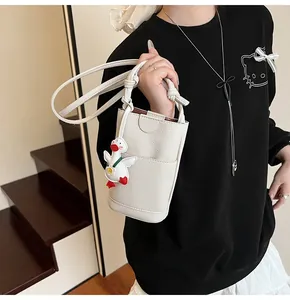 Detail van gebroken witte mini-tas met lychee-textuur, geknoopte riem en eendenbedeltje