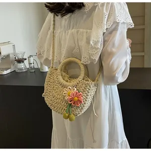 Detail of hand-woven beige straw bag with floral charms and drawstring closure for beach