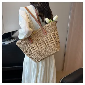 Close-up of woven straw tote bag with brown leather handles and textured bobble stitch detail