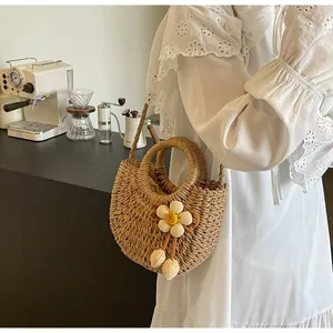 Detail of hand-woven straw bag with floral charm worn on a white lace dress in a cafe
