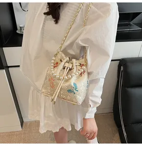 Detailed embroidery on off-white bucket bag with pearl handle and golden chain strap