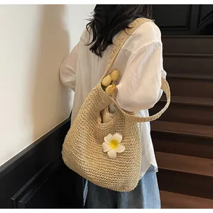 Detail of hand-woven beige straw hobo tote with a white floral charm on a model