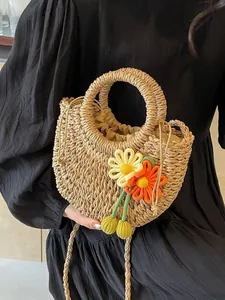 Handwoven straw shoulder bag in semi-circle shape with floral charms and drawstring